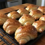 Freshly baked mini croissants on a rustic wooden table.